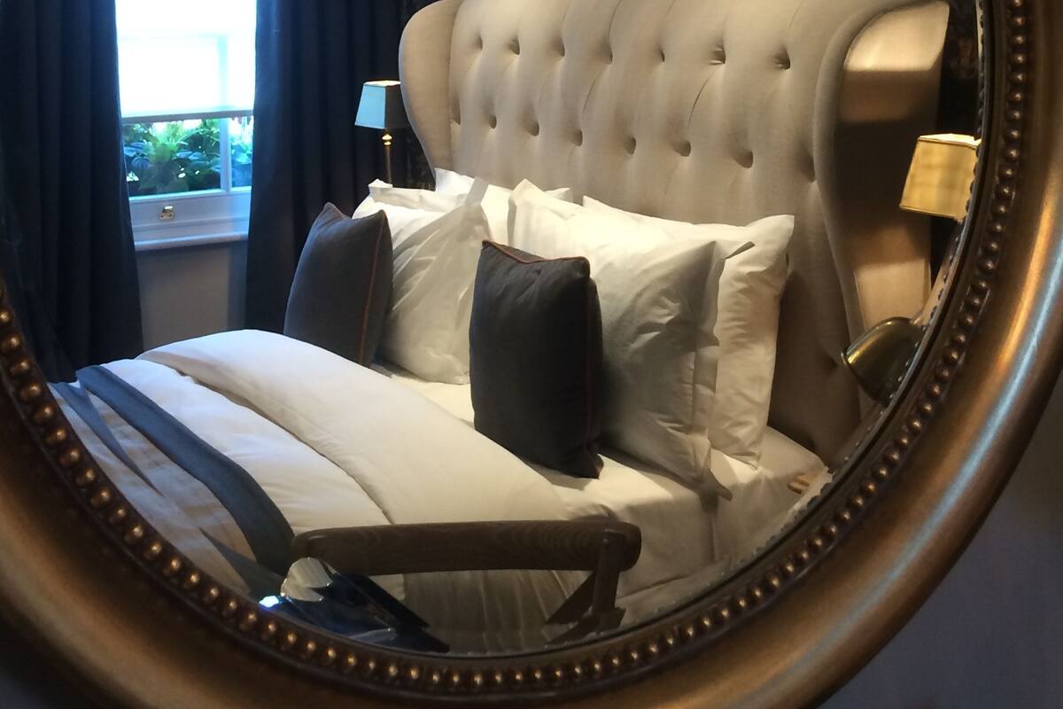 A bedroom with a tufted headboard, a bed with white linens, a nightstand with a lamp, and a window with curtains.