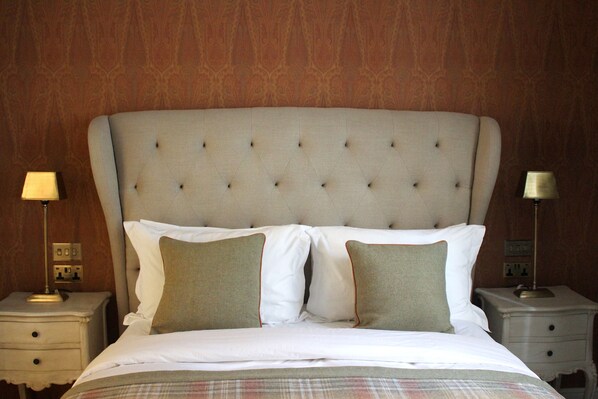 A neatly made bed with a tufted headboard, two bedside tables with lamps, and a patterned wall. - The Hayden Pub & Rooms (London)