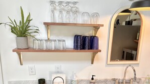 Une cuisine avec un plan de travail en bois, un lave-vaisselle Bosch, un évier et un miroir au-dessus. On y trouve des étagères avec de la verrerie et une plante en pot.