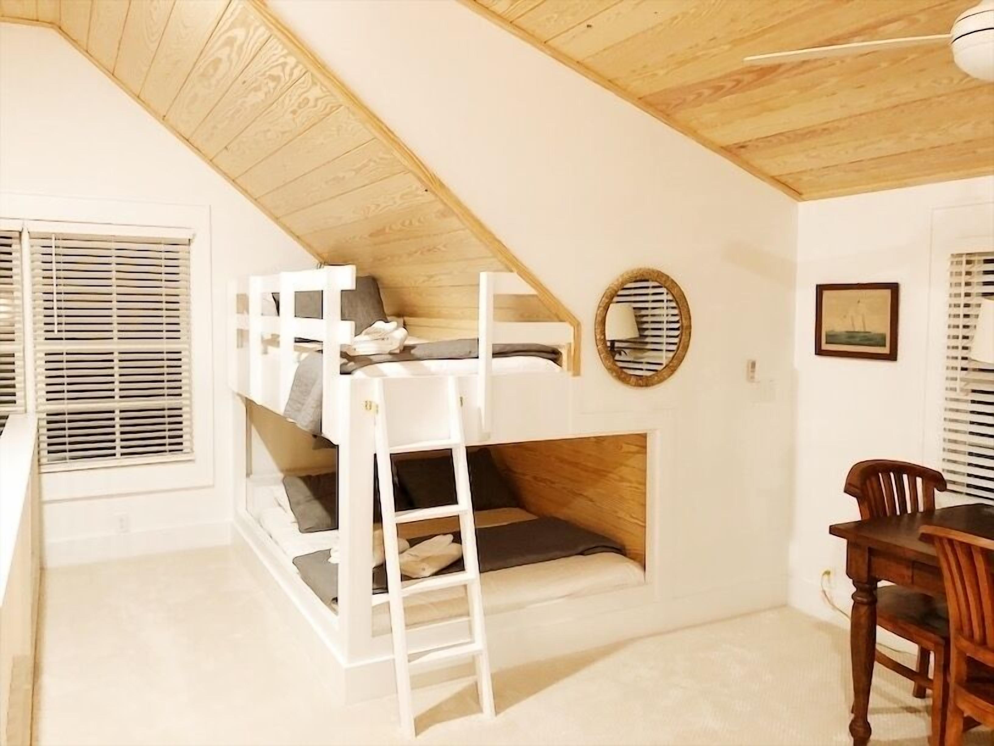 Une pièce avec un lit superposé, un plafond en bois, une table à manger avec des chaises et une fenêtre avec des stores.