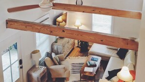 Un loft spacieux avec des poutres apparentes, un grand ventilateur de plafond et un coin salon confortable avec un canapé et des fauteuils.