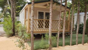 Une cabane en bois dotée d’une terrasse, entourée d’arbres et d’une pelouse.