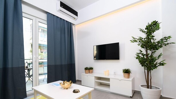 A modern hotel room with a white TV mounted on the wall, a white console table, a potted plant, and a yellow patterned rug. - 45m2 homm Renovated Flat in Neos Kosmos Roumpesi str (Athens)