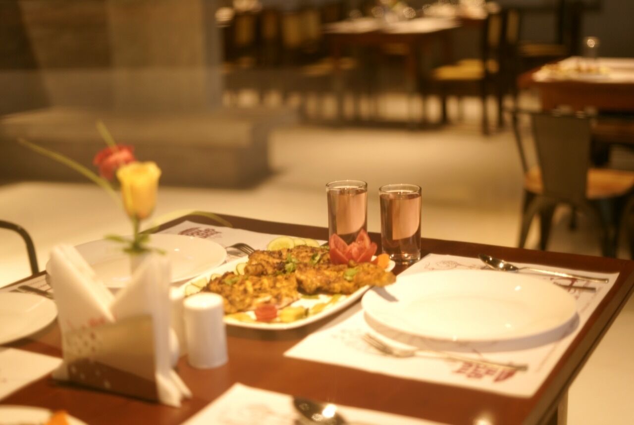 A dining table with a plate of food, two glasses of a beverage, a flower, and a napkin holder.