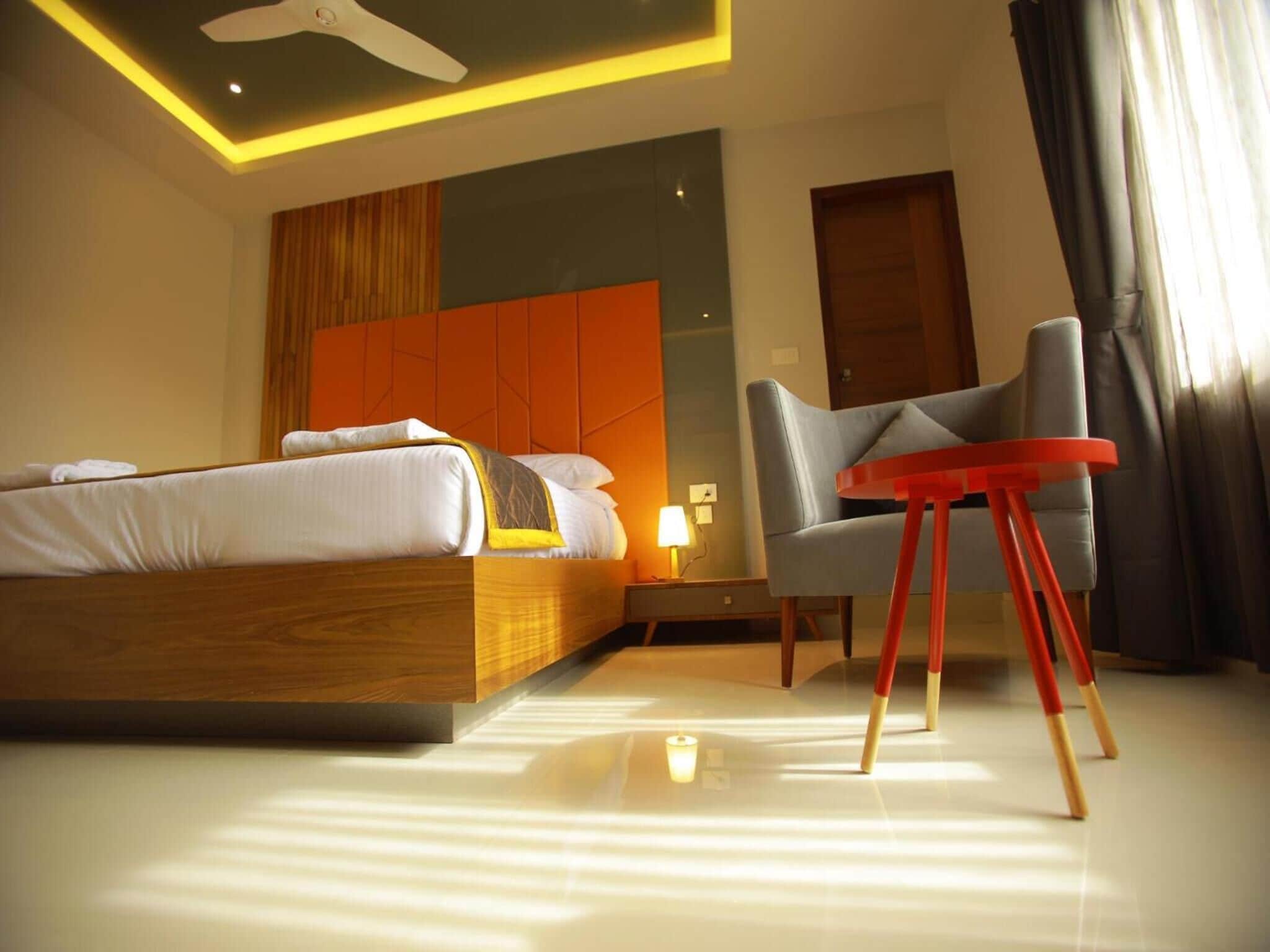 A modern hotel room with a wooden bed, a grey armchair, and a red side table.