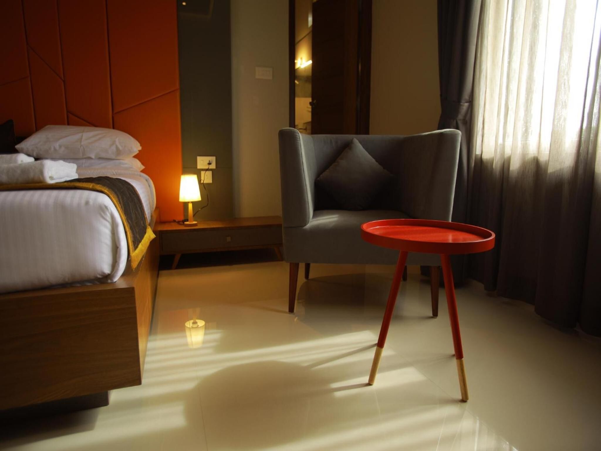 A hotel room with a bed, a chair, a small table, and a nightstand with a lamp.