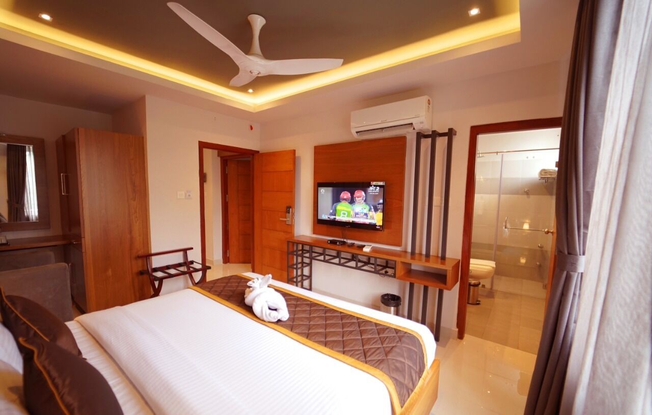 A hotel room with a bed, a TV, a ceiling fan, and a bathroom visible through an open door.
