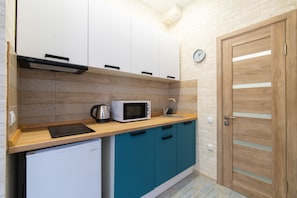 Compact kitchen with microwave, induction cooktop, and refrigerator, set against a backdrop of teal cabinets and a brick-patterned wall.
