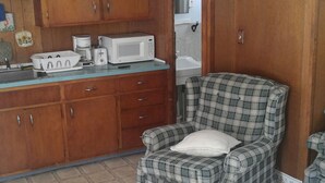 A kitchen with wooden cabinets, a microwave, and a plaid armchair. - 2 bedroom cottages ocean views from property (Hampton)