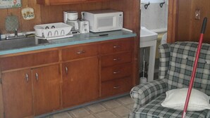 A kitchen with wooden cabinets, a microwave, a coffee maker, and a plaid sofa with a broom. - 2 bedroom cottages ocean views from property (Hampton)