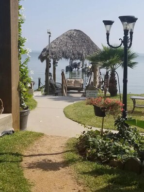 A pathway leading to a thatched-roof structure by the water, with a sign indicating no glass containers. - Awesome 2B/2B cottage on shared waterfront property, 275' pier, pool & hot tub (Bacliff)