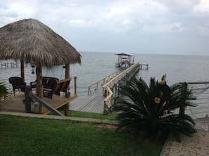 A wooden deck with a thatched roof, overlooking a calm sea.