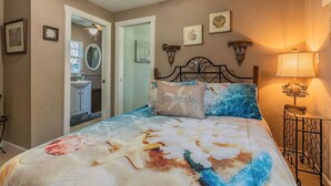 Une chambre à coucher comprenant un lit, une table de chevet, une lampe et une porte donnant sur une salle de bain.