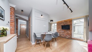 A modern kitchen with a dining area, featuring a brick wall, a flat-screen TV, and a large window. - Barbakan Residence Old Town (Kraków)