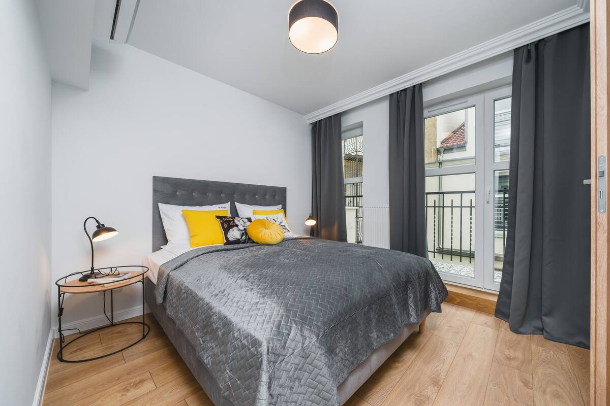 Un dormitorio moderno con cama, mesita de noche, lámpara y vistas al exterior.