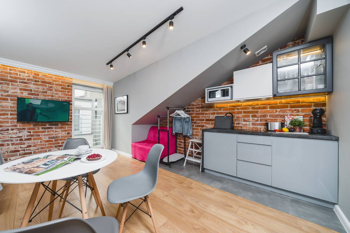 Una cocina moderna con pared de ladrillo, comedor con mesa y sillas, y encimera de cocina con electrodomésticos.