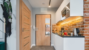 A narrow hallway leading to a wooden door, a kitchen with a brick wall, and a microwave above the counter. - Barbakan Residence Old Town (Kraków)