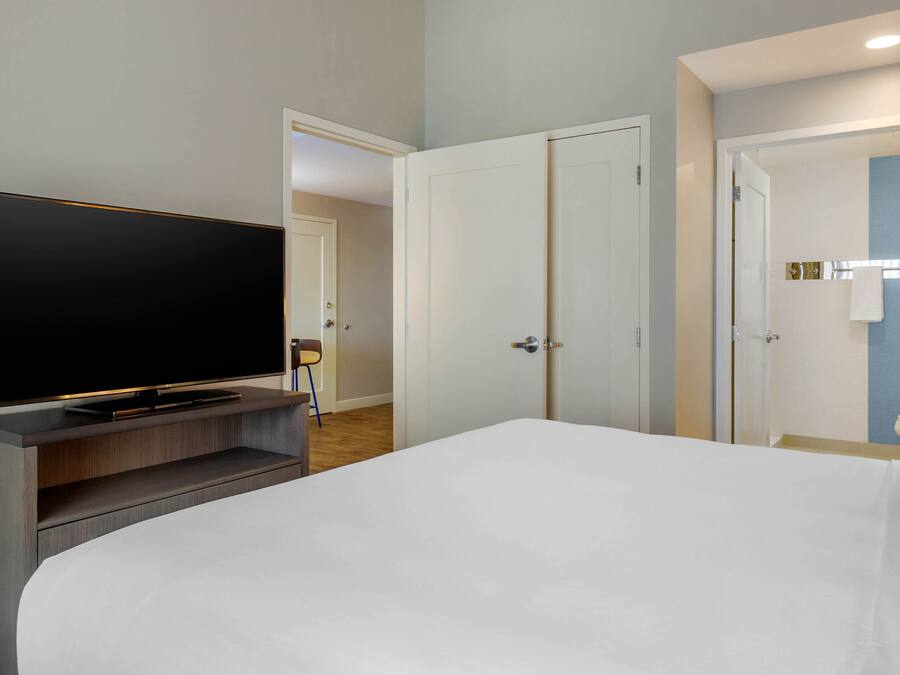 A hotel room with a large bed, a flat-screen TV on a wooden console, and two doors leading to other rooms.
