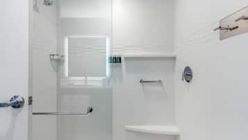 A modern bathroom with white tiles, a glass shower enclosure, a vanity with a mirror, and a small window.