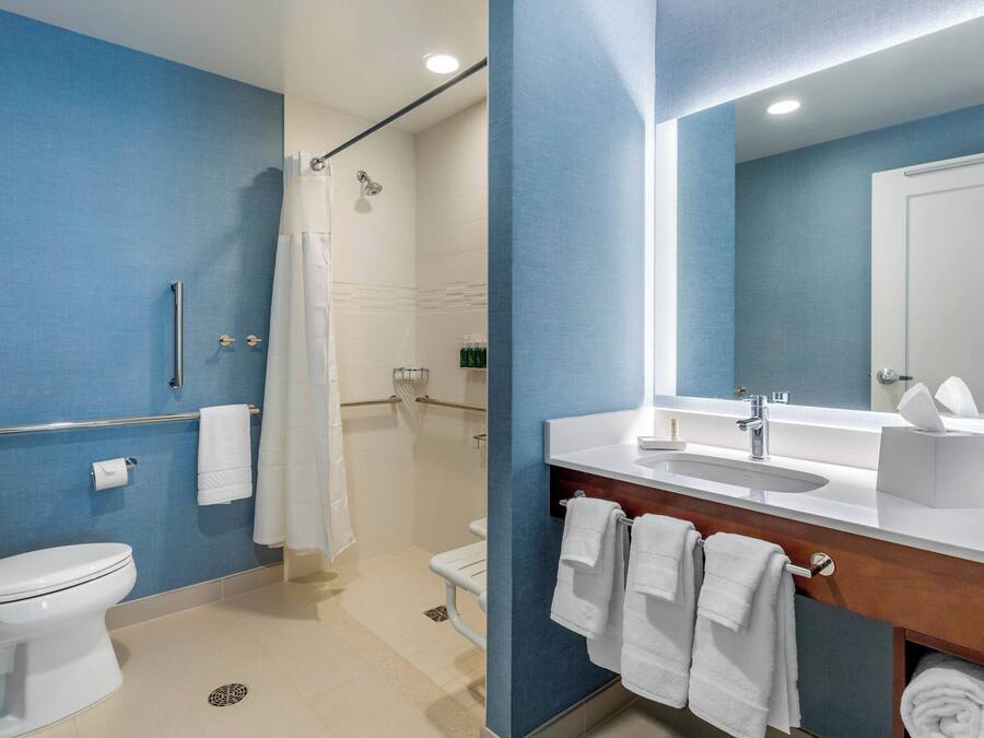 A modern bathroom with a blue accent wall, a white sink, a mirror, and a shower area.