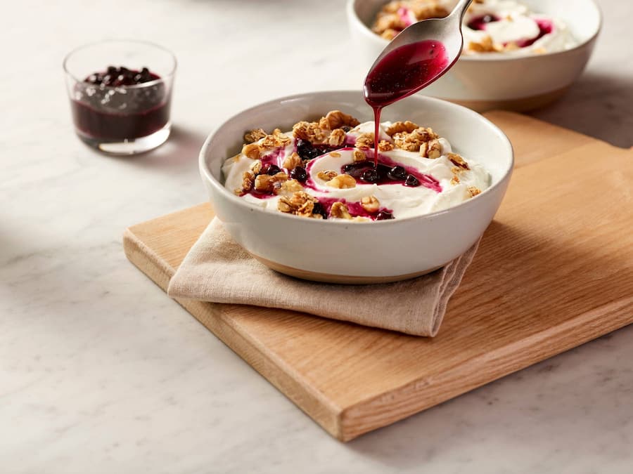 A bowl of yogurt with granola and berries on a wooden board.