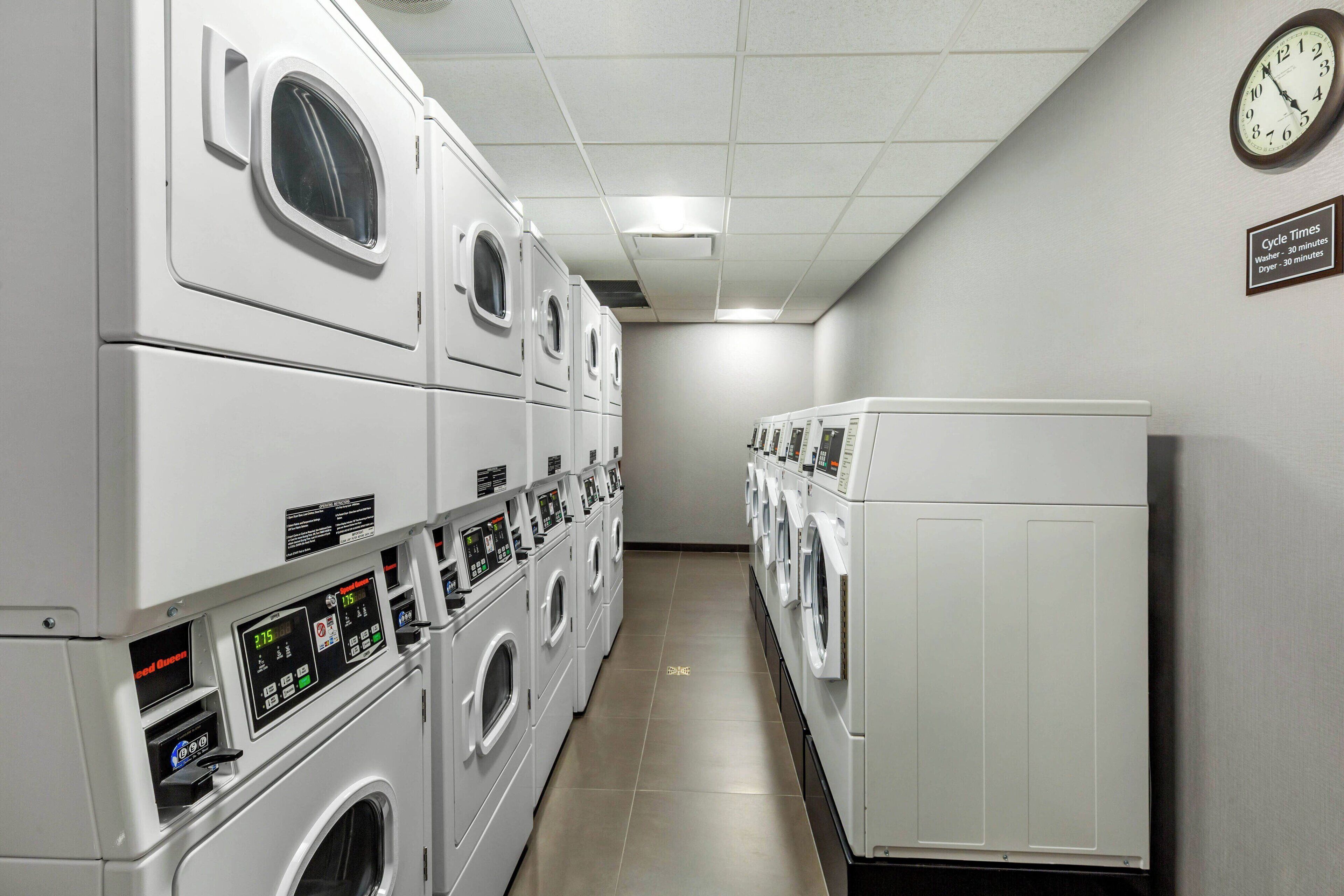 Een wasserette met meerdere wasmachines en drogers, een klok en een bord waarop de wascyclusduur staat vermeld.