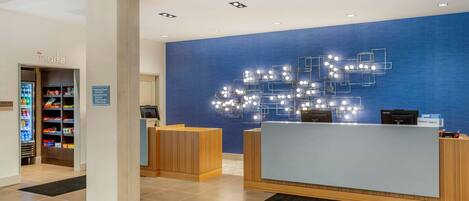 Ein Hotel-Empfangsbereich mit blauer Wand, einer modernen Leuchte und einem Verkaufsautomaten.
