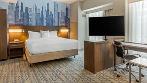 Habitación de hotel con cama, escritorio, silla, televisor y un mural de paisaje urbano en la pared.