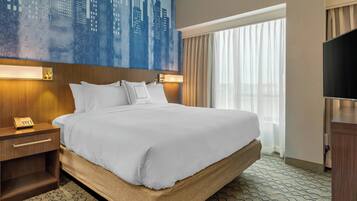 A hotel room with a large bed, a nightstand with a telephone, a flat-screen TV, and a cityscape painting on the wall.