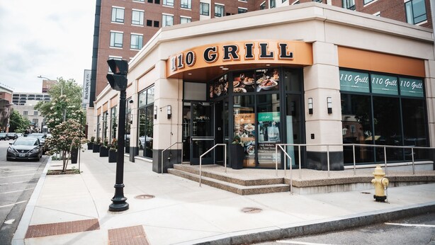 Un restaurante llamado "110 Grill" con una fachada moderna, grandes ventanales y un hidrante en la acera.