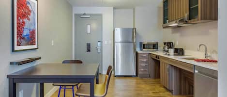 A modern kitchen with a stainless steel refrigerator, wooden cabinets, and a dining area with a table and chairs.