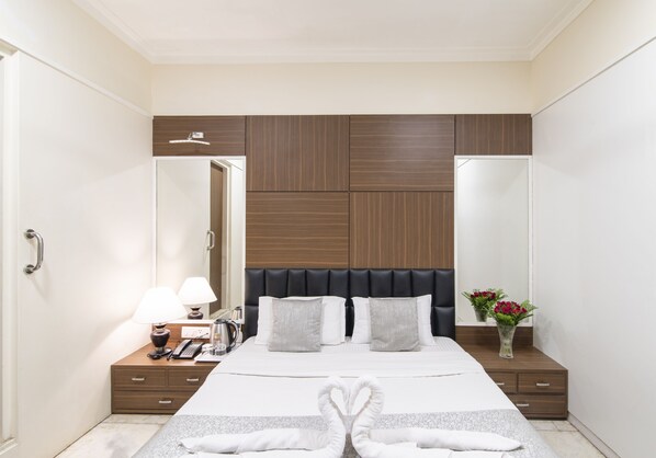 Una camera d'albergo moderna con un letto grande, una testiera in legno, un comodino con una lampada, uno specchio e un vaso con fiori.