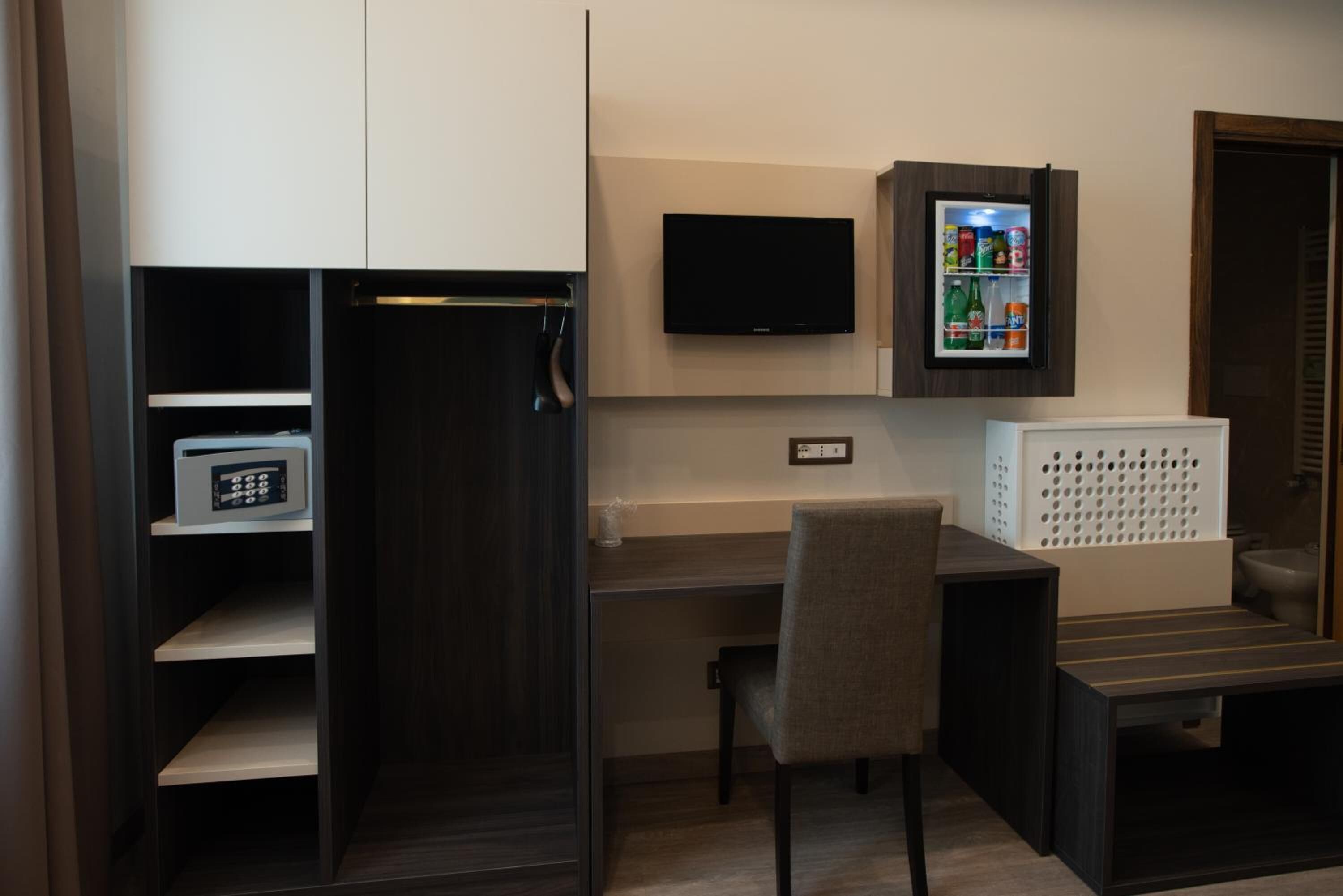Een moderne kamer met een bureau, stoel, televisie en een minibar.