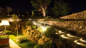 Een aangelegde tuin met stenen muren, een verhard pad en verlichte tuinlampen.