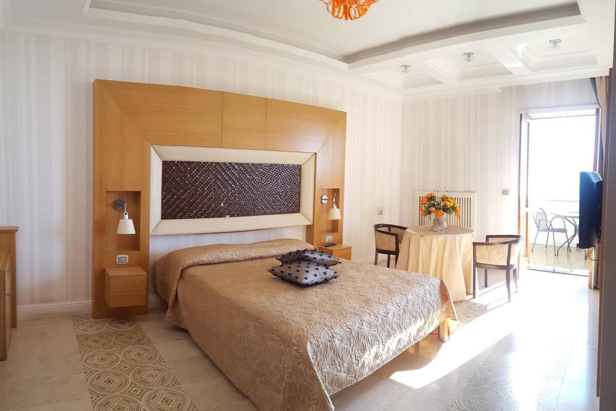 A spacious bedroom with a large bed, a bedside table, a lamp, and a view of a balcony.