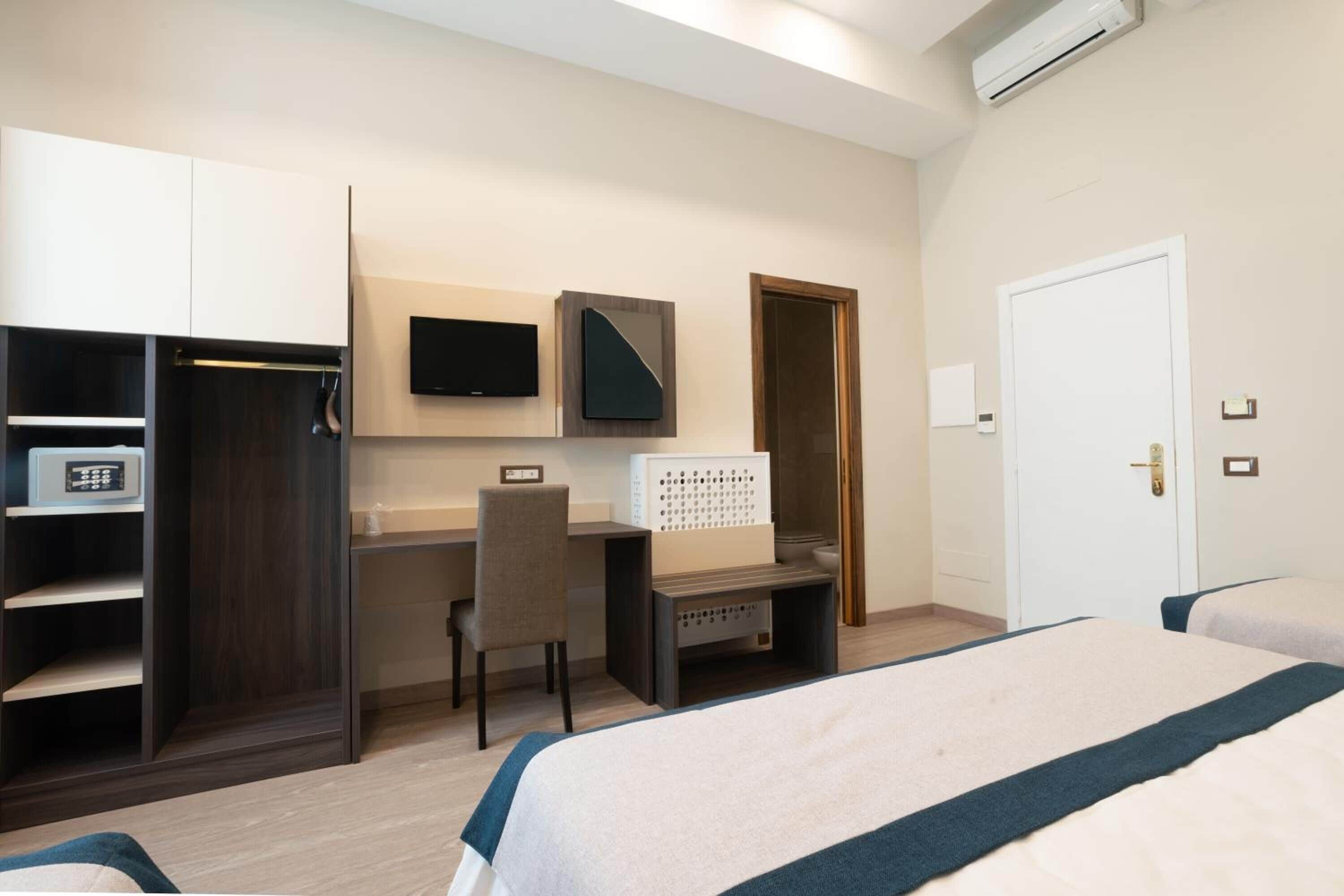 A hotel room with a bed, a desk, a chair, a TV, and a wardrobe.