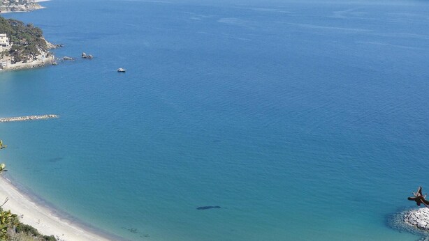 Blick auf die Küste mit blauem Meer, Sandstrand und einem Felsen.