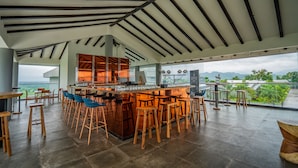 A modern bar area with a high ceiling, wooden stools, and a view of the landscape. - The Forest Club Resort (Karjat)