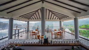 A restaurant with a terrace overlooking a scenic view, featuring wooden tables and chairs, and a variety of glassware on the counter. - The Forest Club Resort (Karjat)