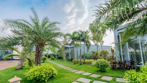 A well-maintained garden with palm trees, a stone pathway, and a small decorative building. - The Forest Club Resort (Karjat)