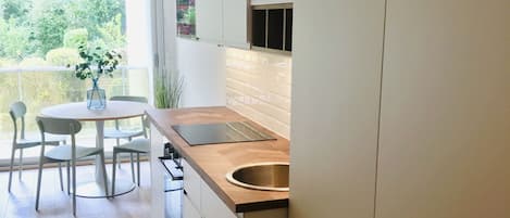 A modern kitchen with a round dining table, white cabinets, and a large window.