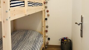 Una litera con ropa de cama a rayas, un picaporte en la pared y un cesto de basura pequeño.