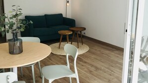 Un espacio de estar moderno con piso de madera, un sofá verde, una mesa de comedor redonda con sillas y una pequeña mesita auxiliar.