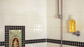 Un baño con ducha, dispensador de jabón y un azulejo decorativo con una figura.