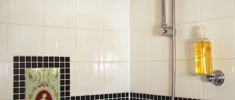 Un baño con ducha, dispensador de jabón y un azulejo decorativo con una figura.