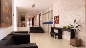 A modern lobby with a staircase, black seating, a reception desk, and a potted plant. - Hotel Skalla (Teixeira de Freitas)