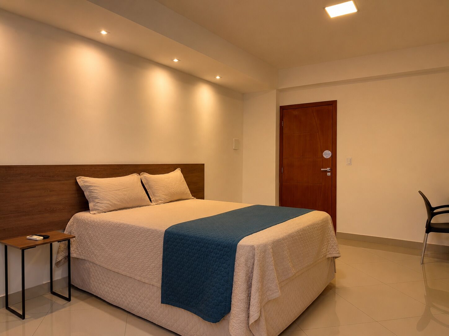 A bedroom with a bed, a nightstand, a chair, and a door.