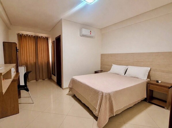 Habitación de hotel con cama, mesita de noche, escritorio, silla y cortinas.