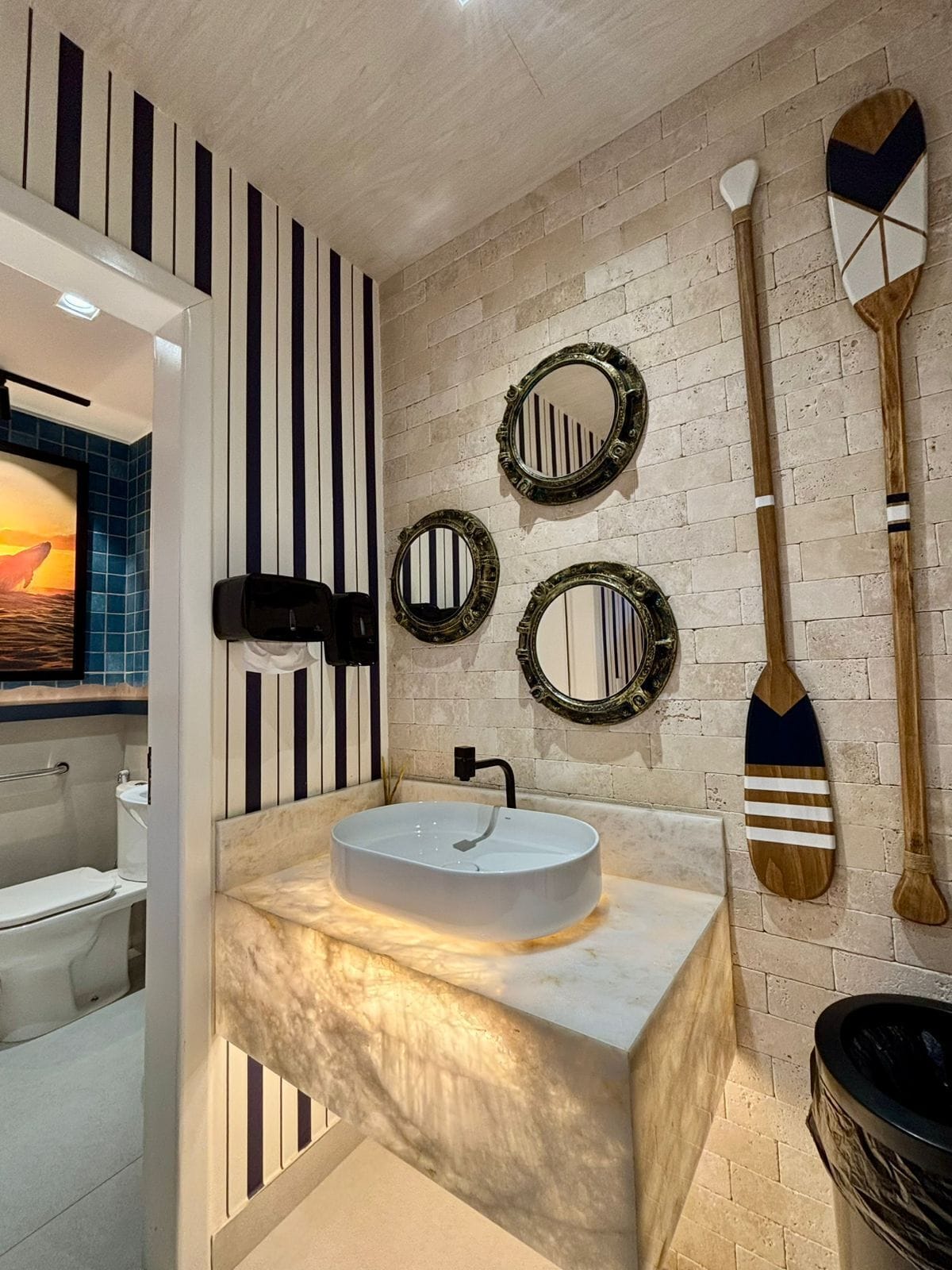 Une salle de bain avec un lavabo en marbre, des motifs rayés sur les murs et plusieurs miroirs.