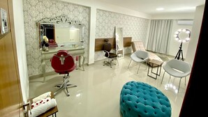 Une chambre moderne avec une coiffeuse, des miroirs, un fauteuil rouge, un fauteuil blanc, un pouf bleu et un anneau lumineux.